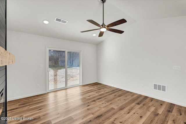 empty room with ceiling fan, a fireplace, vaulted ceiling, and light wood-type flooring