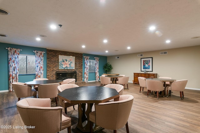 dining room featuring a brick fireplace, a textured ceiling, and light hardwood / wood-style flooring