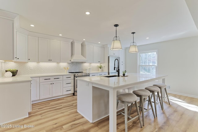 kitchen featuring white cabinets, premium range hood, a center island with sink, and stainless steel range