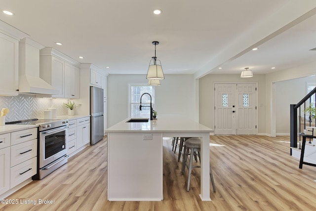 kitchen featuring sink, decorative light fixtures, an island with sink, stainless steel appliances, and white cabinets