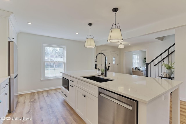 kitchen featuring a kitchen island with sink, sink, stainless steel dishwasher, and white cabinets