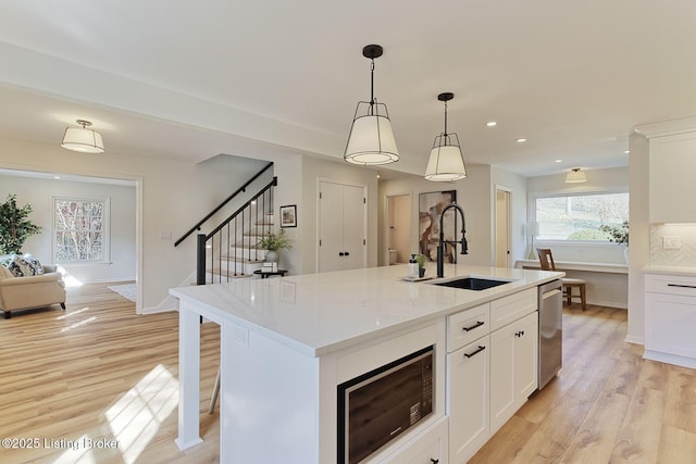 kitchen featuring white cabinetry, sink, decorative light fixtures, and an island with sink