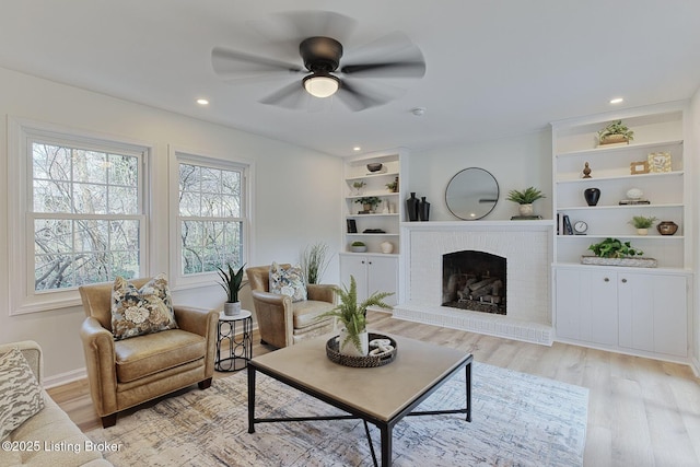 living room with ceiling fan, built in features, a fireplace, and light hardwood / wood-style floors