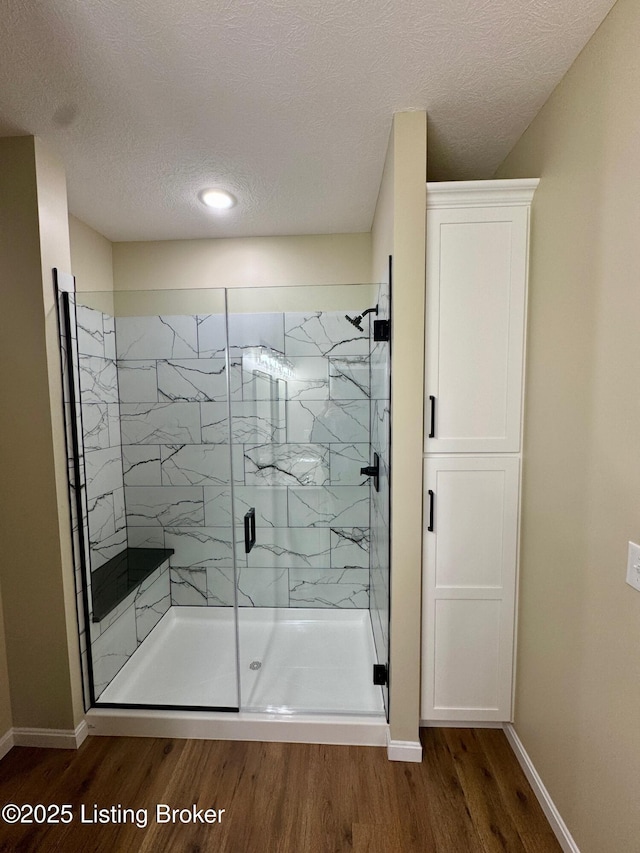 bathroom with hardwood / wood-style floors, a textured ceiling, and a shower with shower door