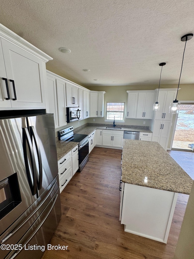 kitchen with dark wood-type flooring, a center island, hanging light fixtures, stainless steel appliances, and white cabinets
