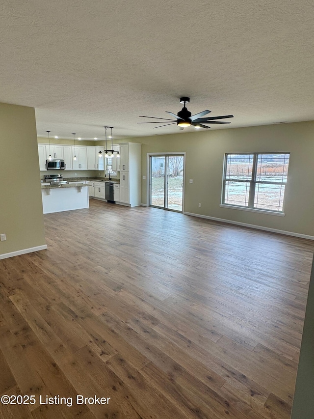 unfurnished living room featuring hardwood / wood-style flooring, ceiling fan, and a textured ceiling