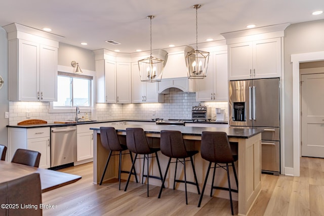 kitchen featuring appliances with stainless steel finishes, hanging light fixtures, a kitchen breakfast bar, a center island, and custom range hood