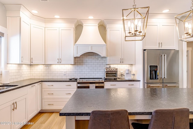 kitchen featuring stainless steel appliances, premium range hood, a kitchen bar, and decorative light fixtures