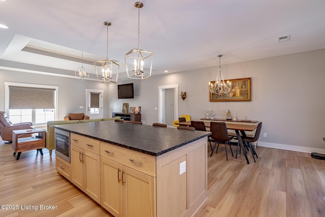 kitchen featuring hanging light fixtures, a raised ceiling, stainless steel microwave, and light wood-type flooring