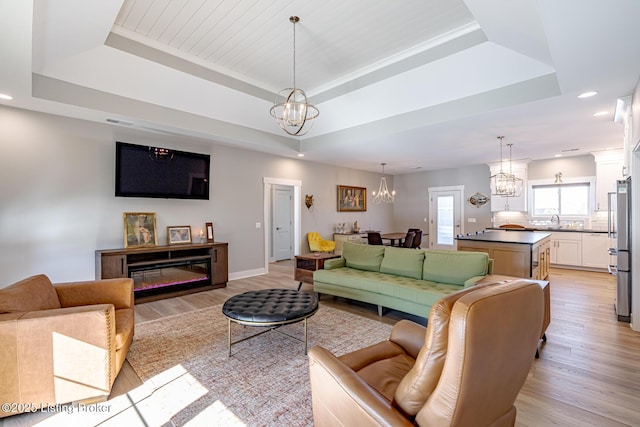 living room featuring a raised ceiling, light wood-type flooring, and a chandelier