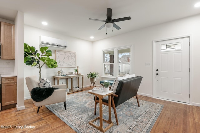 sitting room featuring ceiling fan, an AC wall unit, and light wood-type flooring