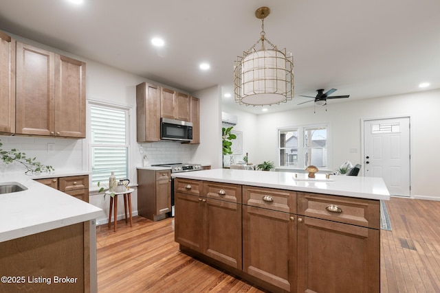 kitchen with decorative light fixtures, light wood-type flooring, a center island, and appliances with stainless steel finishes