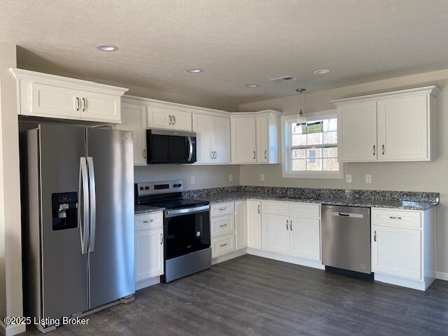 kitchen featuring appliances with stainless steel finishes, dark hardwood / wood-style floors, dark stone countertops, and white cabinets