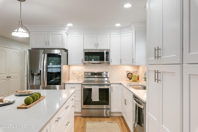 kitchen featuring appliances with stainless steel finishes, decorative light fixtures, white cabinetry, backsplash, and light wood-type flooring