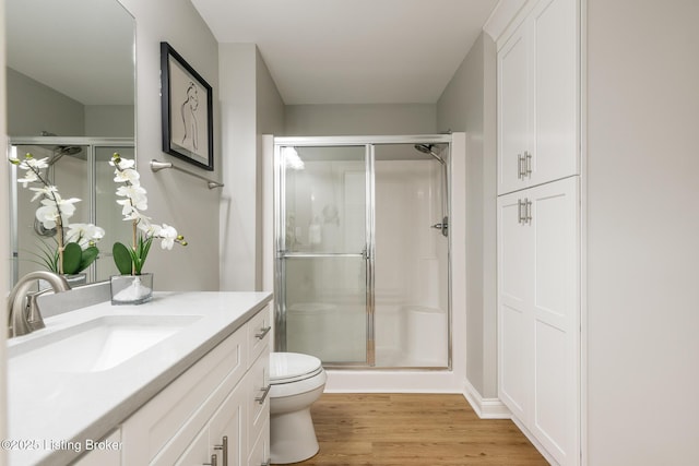 bathroom featuring wood-type flooring, toilet, a shower with door, and vanity