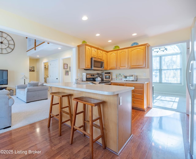 kitchen featuring appliances with stainless steel finishes, sink, a kitchen bar, light hardwood / wood-style floors, and kitchen peninsula