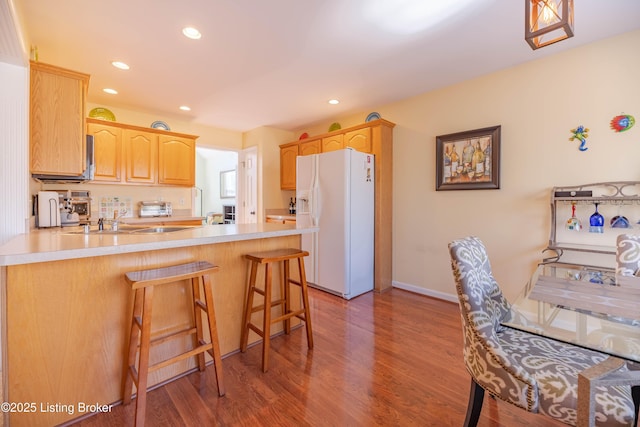 kitchen featuring wood-type flooring, a kitchen breakfast bar, white refrigerator with ice dispenser, kitchen peninsula, and light brown cabinets