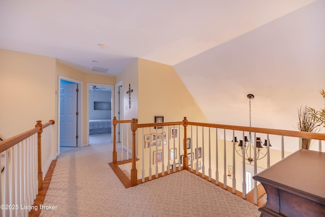 hallway featuring an inviting chandelier, vaulted ceiling, and light carpet