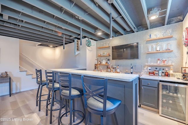 bar with tasteful backsplash, gray cabinetry, beverage cooler, and light stone counters