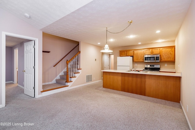 kitchen with appliances with stainless steel finishes, a textured ceiling, light carpet, decorative light fixtures, and kitchen peninsula