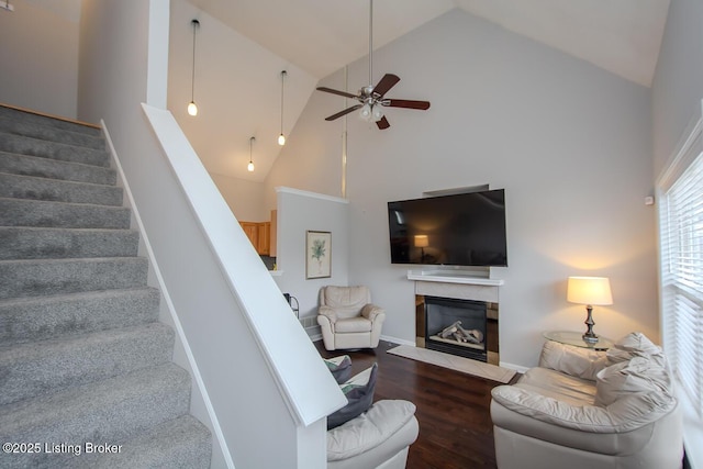 living room with dark wood-type flooring, ceiling fan, a high end fireplace, and high vaulted ceiling