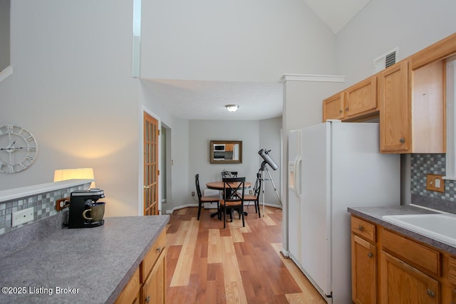 kitchen with tasteful backsplash, vaulted ceiling, white fridge with ice dispenser, and light hardwood / wood-style floors