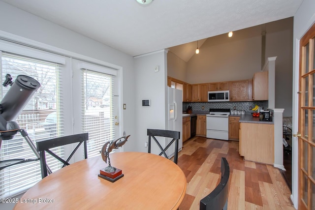 kitchen featuring lofted ceiling, white appliances, tasteful backsplash, and light hardwood / wood-style floors