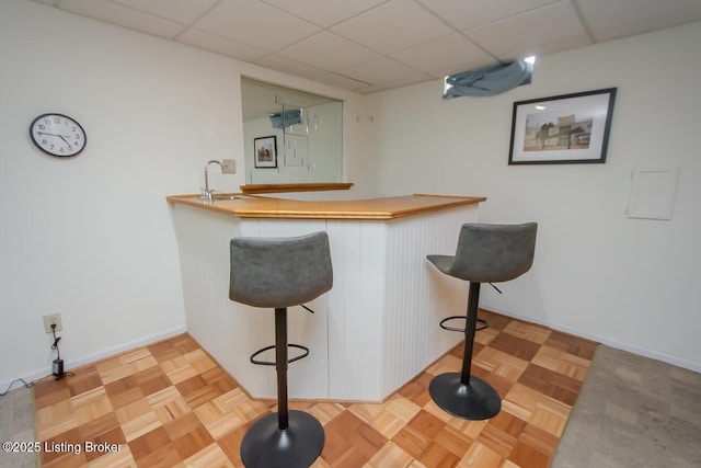 bar featuring light parquet flooring, sink, and a drop ceiling