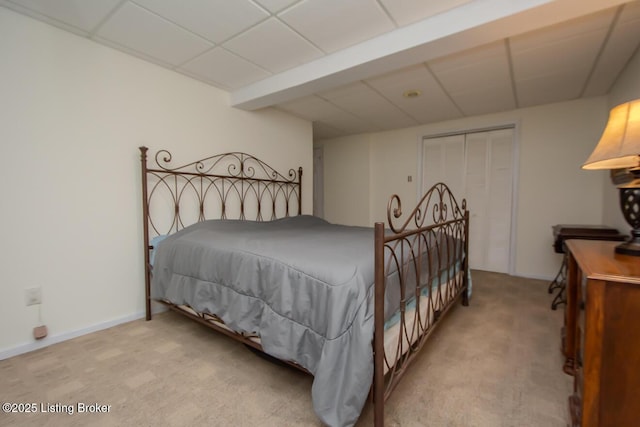 bedroom featuring a drop ceiling, light colored carpet, and a closet