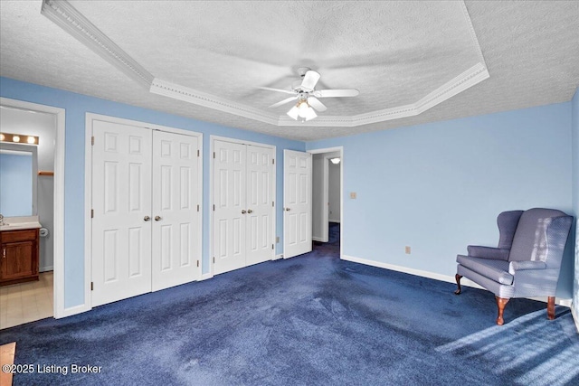 unfurnished bedroom with dark carpet, two closets, a raised ceiling, and a textured ceiling