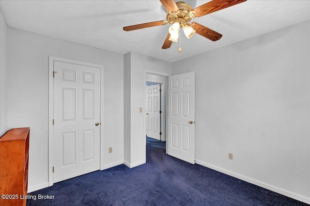 unfurnished bedroom featuring ceiling fan, dark carpet, and a textured ceiling