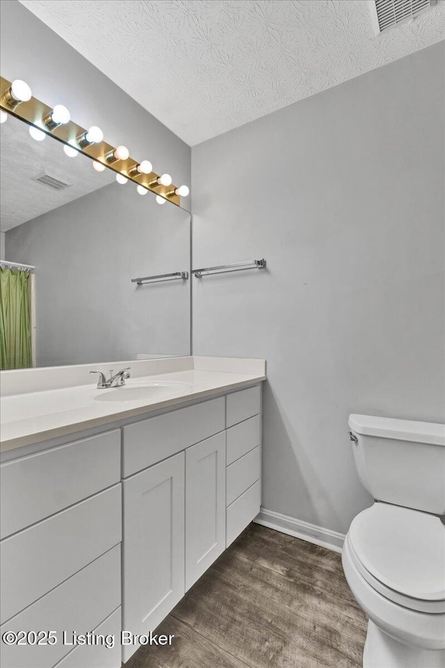 bathroom featuring vanity, wood-type flooring, toilet, and a textured ceiling