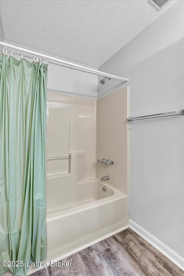 bathroom with hardwood / wood-style floors, a textured ceiling, and shower / bath combo