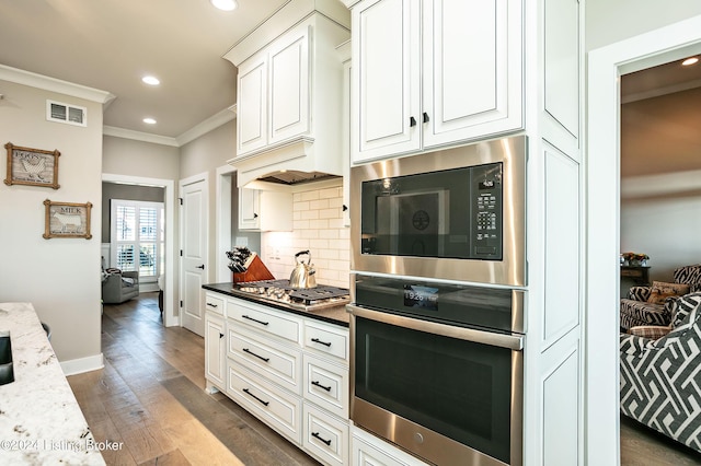 kitchen featuring white cabinetry, crown molding, dark stone counters, stainless steel gas stovetop, and backsplash