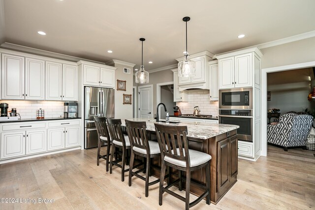 kitchen featuring a breakfast bar, decorative light fixtures, dark stone counters, a kitchen island with sink, and stainless steel appliances