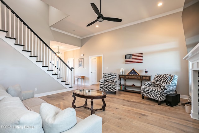 living room with crown molding, ceiling fan, light hardwood / wood-style flooring, and a towering ceiling