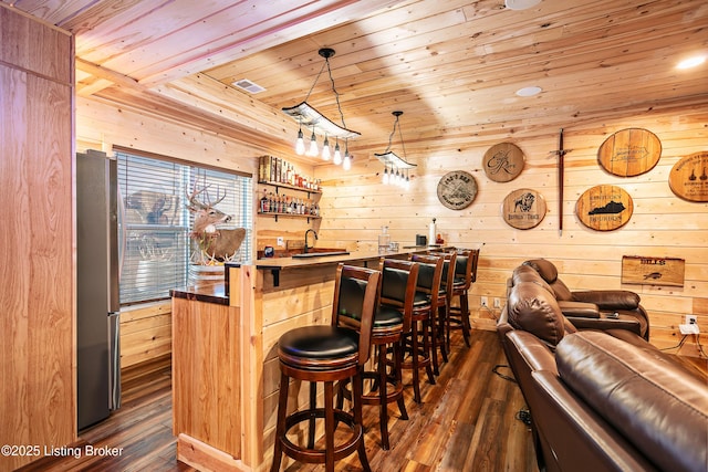 bar featuring dark hardwood / wood-style floors, wooden walls, stainless steel refrigerator, decorative light fixtures, and wooden ceiling