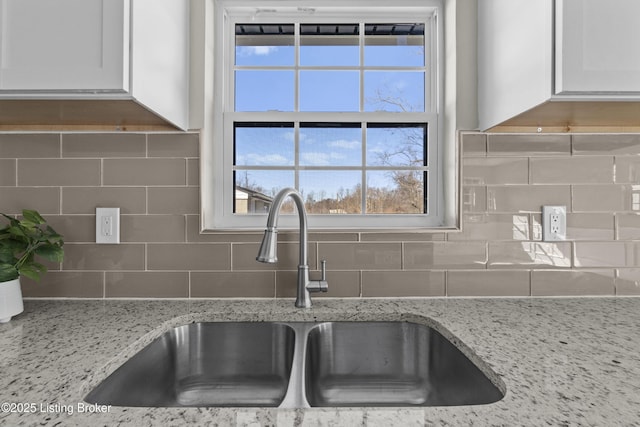 kitchen with white cabinetry, sink, backsplash, and light stone countertops