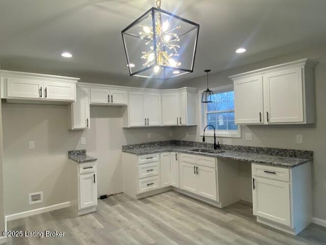 kitchen with hanging light fixtures, light wood-style flooring, a sink, and white cabinetry