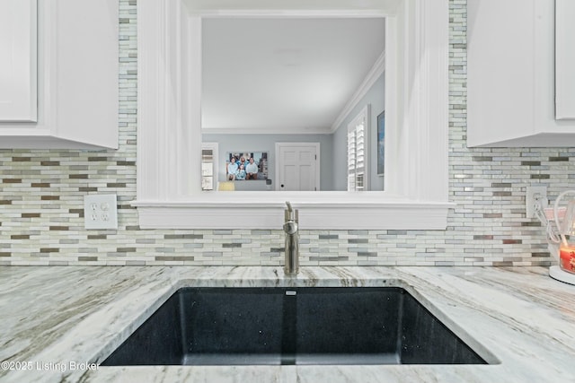 kitchen with ornamental molding, sink, white cabinets, and light stone counters