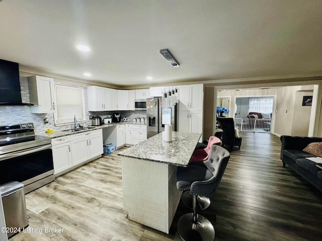 kitchen with appliances with stainless steel finishes, decorative light fixtures, white cabinetry, a kitchen breakfast bar, and a center island