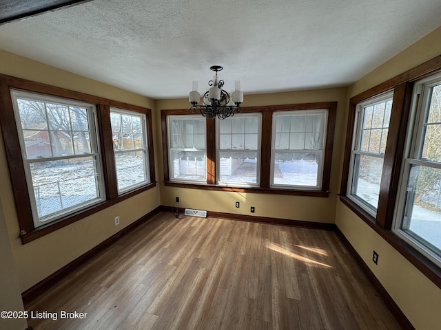 unfurnished dining area with wood finished floors, baseboards, visible vents, a textured ceiling, and a chandelier