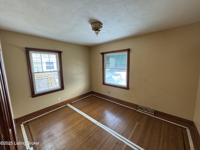 spare room featuring visible vents, a textured ceiling, baseboards, and wood finished floors