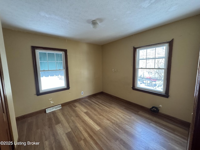 spare room featuring baseboards, wood finished floors, visible vents, and a textured ceiling