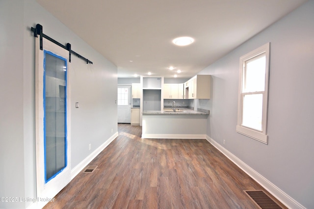 unfurnished living room with a barn door, dark wood-type flooring, and sink