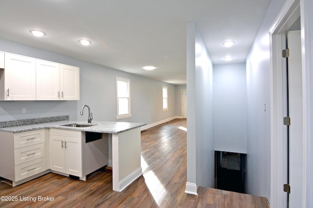 kitchen with light stone counters, sink, kitchen peninsula, and white cabinets