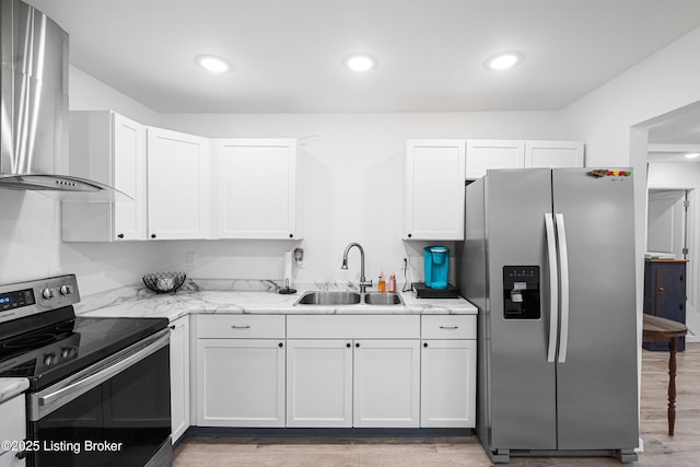 kitchen featuring appliances with stainless steel finishes, sink, white cabinets, light stone countertops, and wall chimney range hood