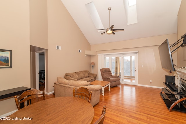 living room with ceiling fan, high vaulted ceiling, light wood-type flooring, and a skylight