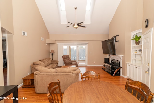 living room with high vaulted ceiling, a fireplace, a skylight, ceiling fan, and light hardwood / wood-style floors