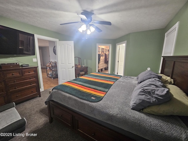 bedroom with dark colored carpet, ceiling fan, a walk in closet, and a textured ceiling